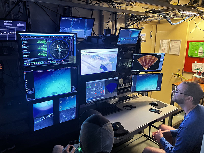 On board Research Vessel Kilo Moana Dr. Andrew Pietruszka, one of the Principal Investigators of the Deepwater Surveys of World War II U.S. Cultural Assets in the Saipan Channel expedition from Scripps Institution of Oceanography, helps guide piloting of a remotely operated vehicle (ROV) that is exploring underwater sites that may contain aircraft wreckage. Dr. Pietruszka is the lead archaeologist of the program. Screens show a live feed from the cameras as well as information on depth and pitch of the ROV. Additionally, a forward-looking sonar is used to guide researchers to objects that are out of the field of view of the cameras.