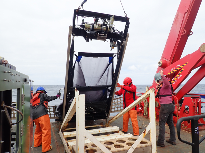 Team members recover the Multiple Opening/Closing Net and Environmental Sensing System (MOCNESS). As seen here, a variety of sensors are attached to the top of the frame to measure environmental parameters (i.e., depth, temperature, salinity, oxygen, etc.) as the system moves through the water column.