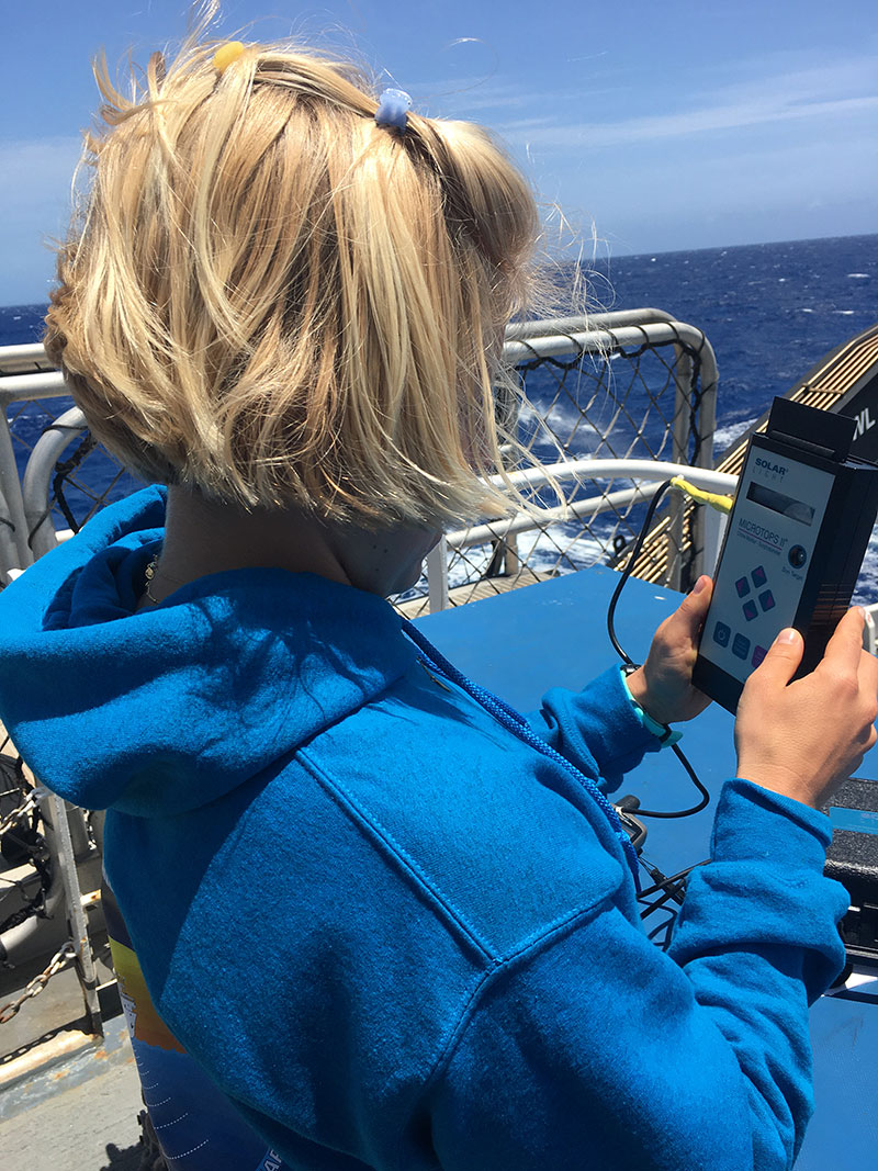Explorer-in-Training Paige Hoel  takes a reading from a sunphotometer during the 2022 Puerto Rico Mapping and Deep-Sea Camera Demonstration. During expeditions on NOAA Ship Okeanos Explorer, in support of a project led by NASA, NOAA Ocean Exploration uses a sunphotometer, a type of light meter, to measure maritime aerosols. These tiny solid and liquid particles are suspended in the atmosphere above the ocean (e.g., windblown dust, sea salts, volcanic ash, smoke from fires, and pollution) and are important to scientists because they can affect climate, weather, and people's health.