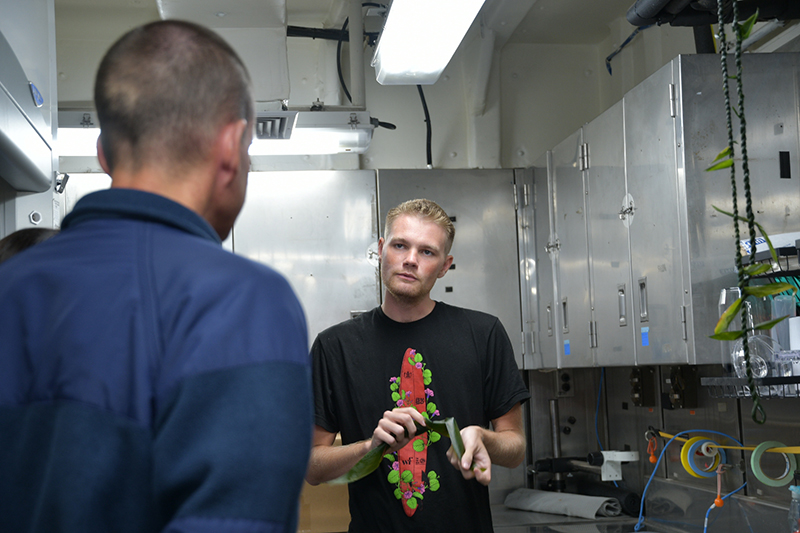 Makoa Pascoe, who is serving as a cultural liaison during the Beyond the Blue: Papahānaumokuākea Mapping 1 expedition, teaches members of NOAA Ship <i>Okeanos Explorer</i>’s crew how to make lei lā’ī of ti leaves. Prior to the ship’s departure, the cultural liaison team prepared a lei lāʻī for placement on the ship’s bridge rail as part of an Oli Pale to seek protection while underway. Many members of the on-ship team hung the lei they made on their stateroom doors.